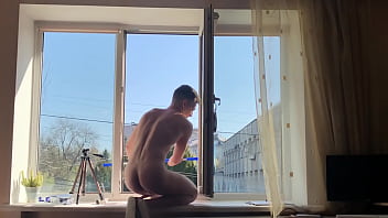Joven limpiador de ventanas completamente desnudo lava las ventanas por la mañana
