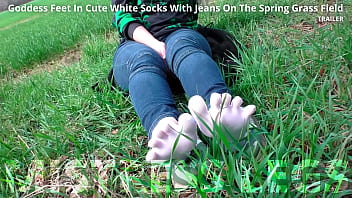 Goddess feet in cute white socks with jeans on the spring grass field